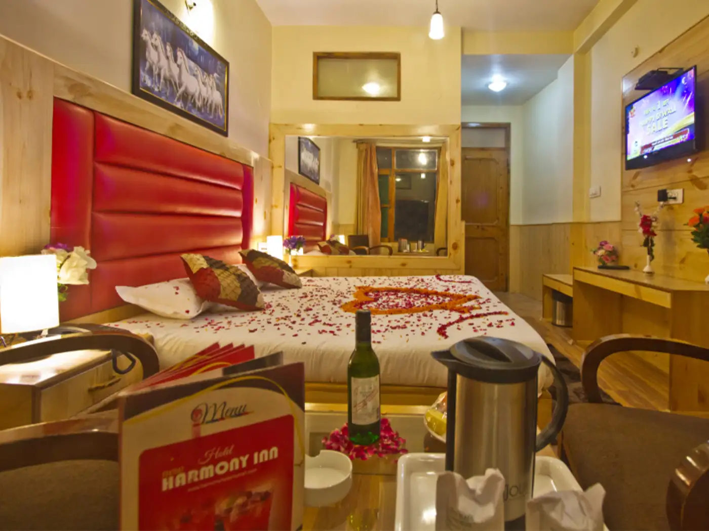Romantic hotel room with rose petals on bed, wine, and menu