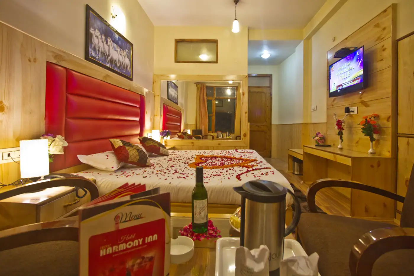 Romantic hotel room with rose petals on bed, wine, and menu