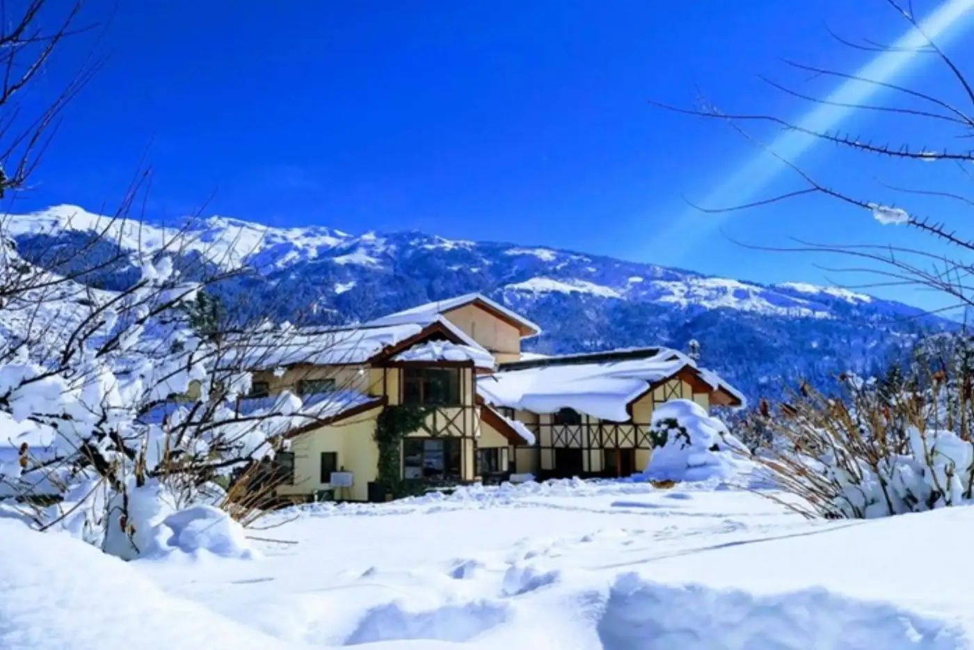 Snow-covered chalet with mountains in the background under a clear blue sky.