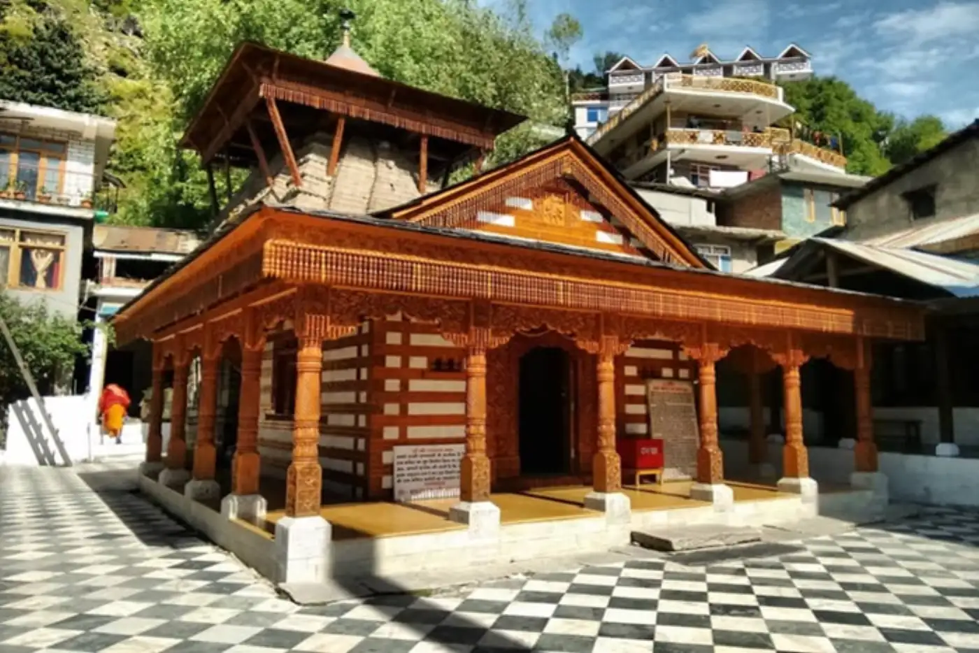 Beautiful wooden temple in Manali, India with checkered floor and mountain backdrop.